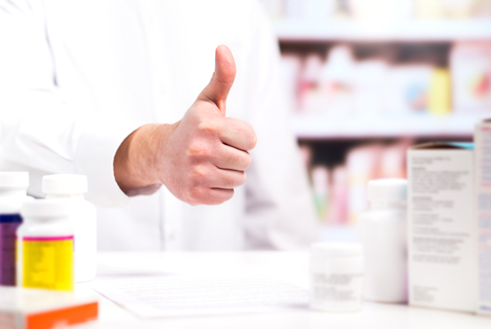 Happy,pharmacist,showing,thumbs,up,at,pharmacy,counter,full,of
